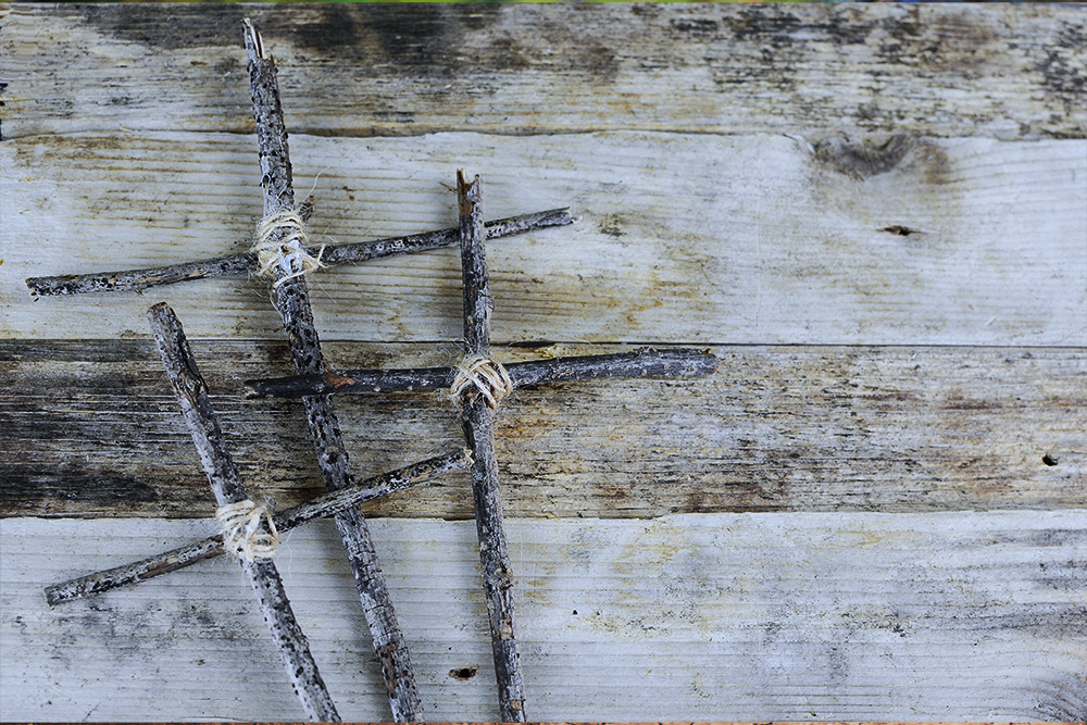 Three crosses made from sticks and twine on a rough wooden background